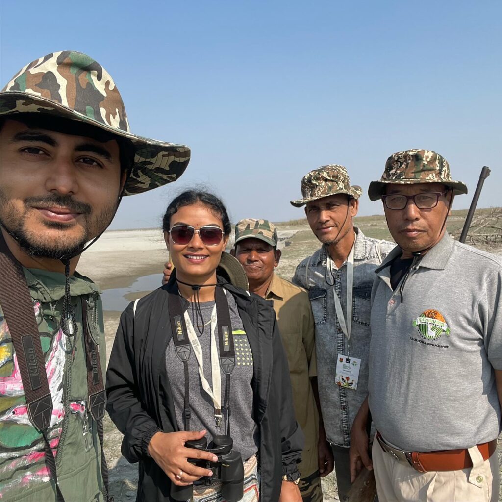 Group of five birding enthusiasts with binoculars and cameras during guided wildlife tour at wetland habitat.