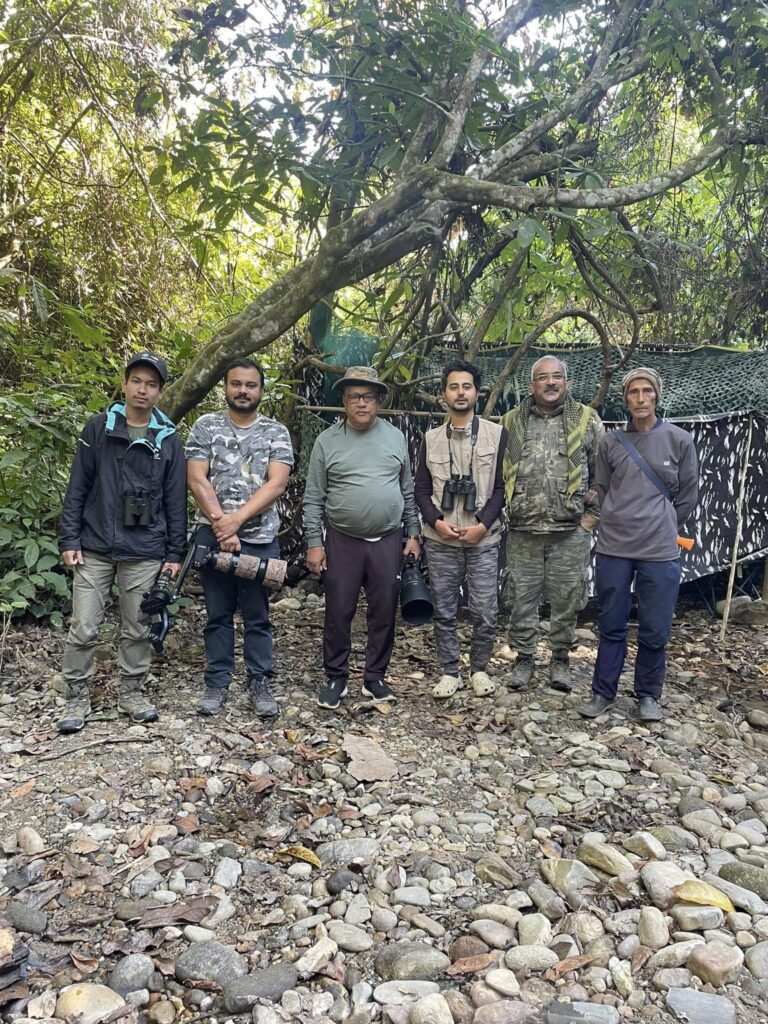 Birding tour participants seated in forest hide with professional camera equipment and telephoto lenses