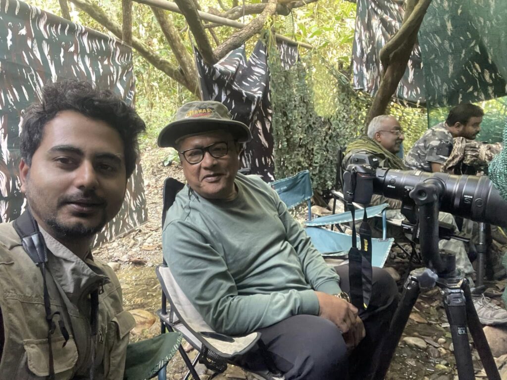 Birding tour participants seated in forest hide with professional camera equipment and telephoto lenses